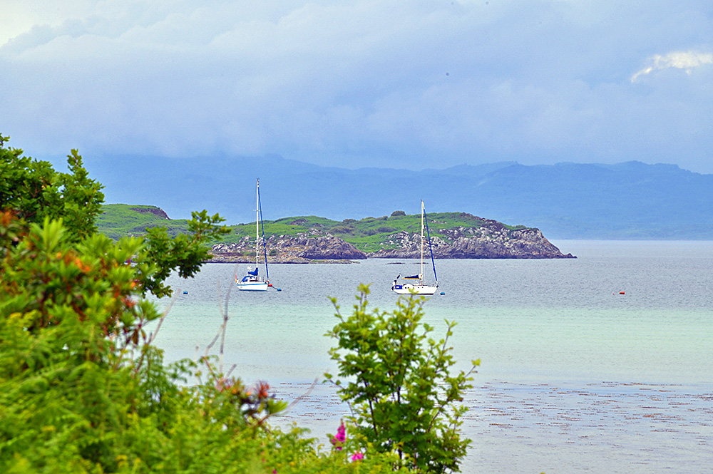 Picture of two sailing yachts moored off the shore of an island, the mainland visible in the background