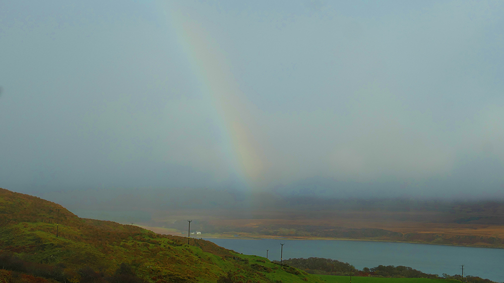 Picture of a faint rainbow on a wet day at a sound between two islands