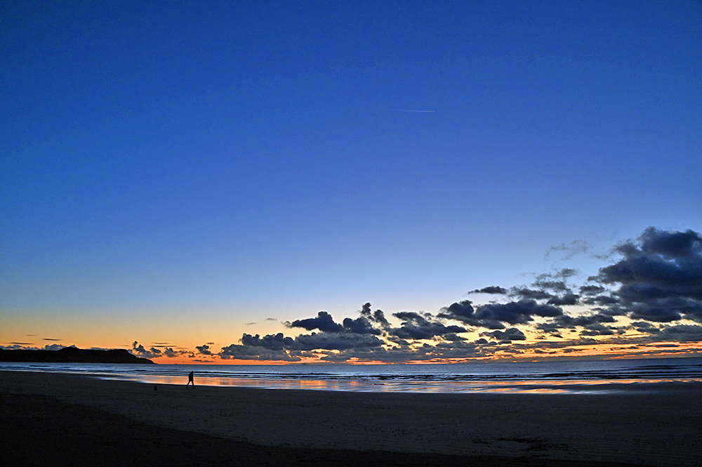 Picture of a man walking along a sandy beach in the last light of the gloaming