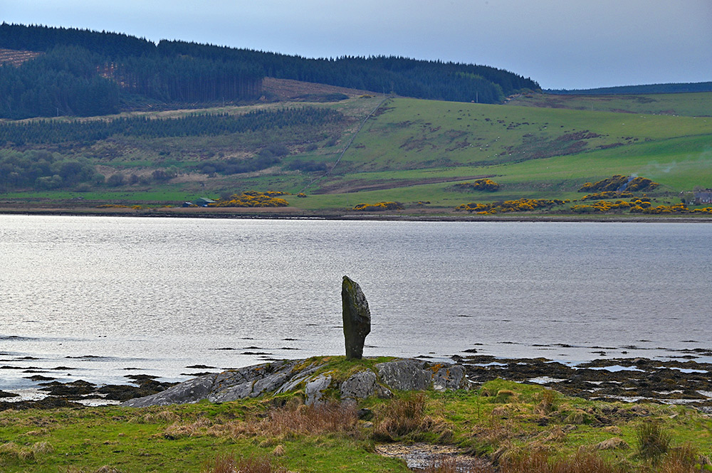 Picture of a standing stone on a rocky outcrop on the shore of a sea loch