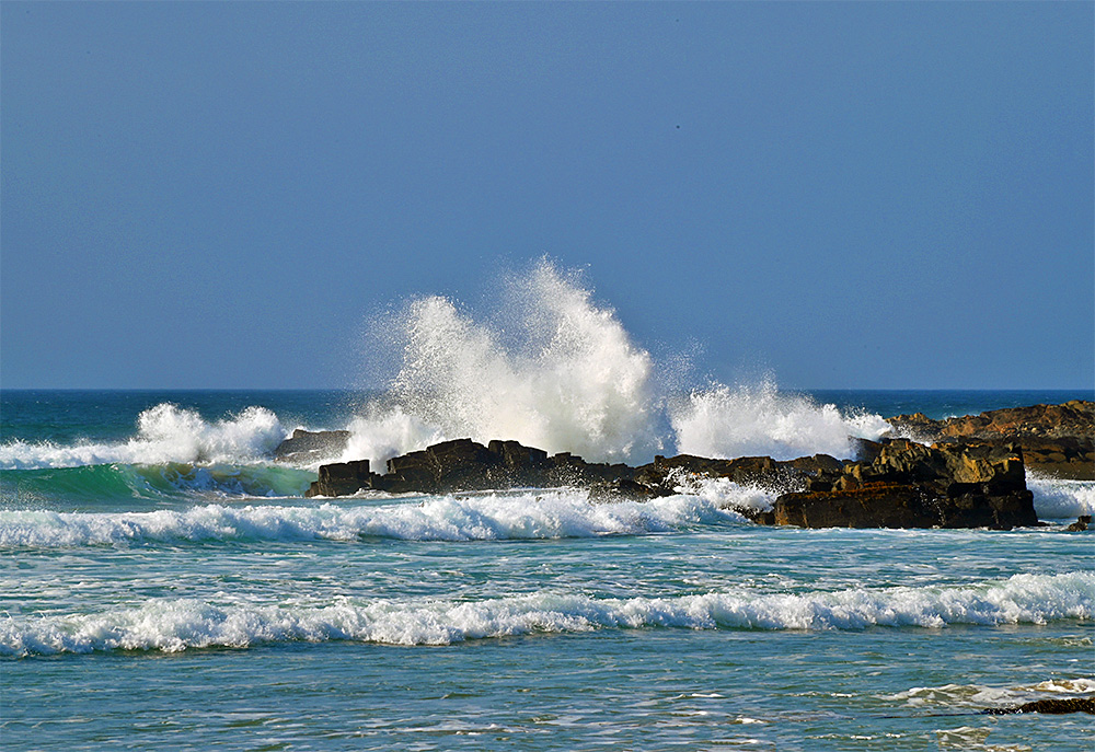 Picture of a wave breaking over coastal rocks, sending a big splash into the air