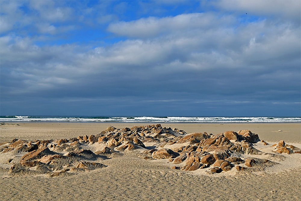 Picture of some rocks in a beach, partially covered by windblown sand