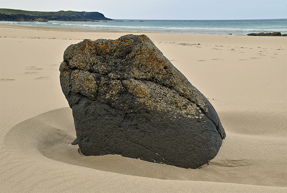 Picture of a rock standing in the sand of a beach in a bay