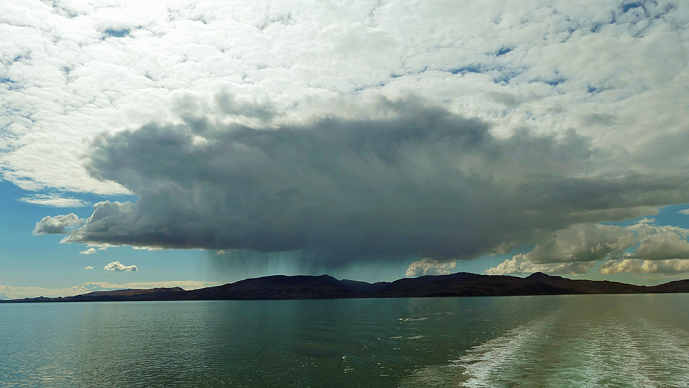 Picture of a dark cloud over an island with some heavy rain falling in one place, seen from a ferry