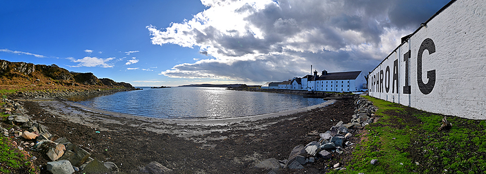 Panoramic picture of Laphroaig distillery on the shore of Loch Laphroaig with a mixture of clouds and sunshine