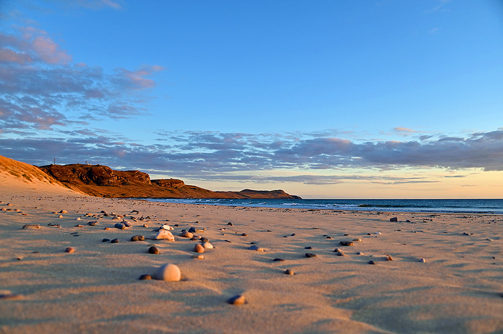 Picture of beach with small pebbles in the sand and crags in the distance. All in some nice sunset light