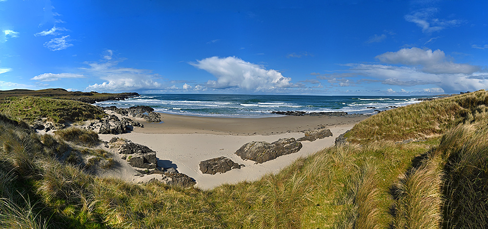 Panoramic picture from a path through dunes on to a beach in a wide bay