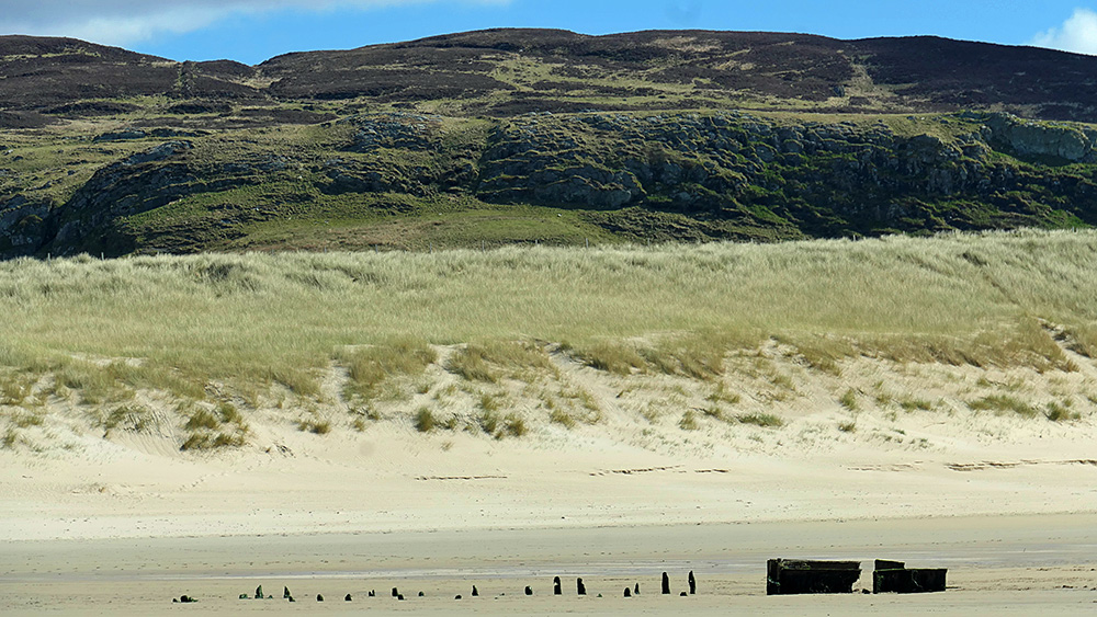 Picture of a wreck on a beach with dunes and crags in the background