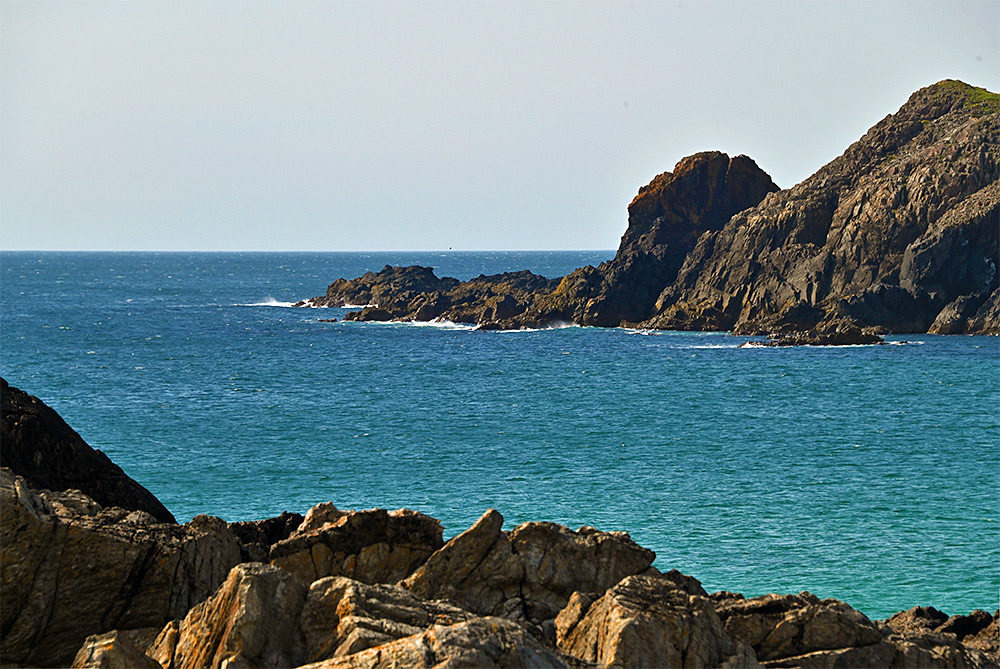 Picture of some dark rocks and cliffs at the entrance to a bay