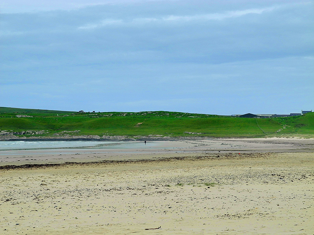 Picture of a long wide beach on a cloudy morning, a lone walker in the distance