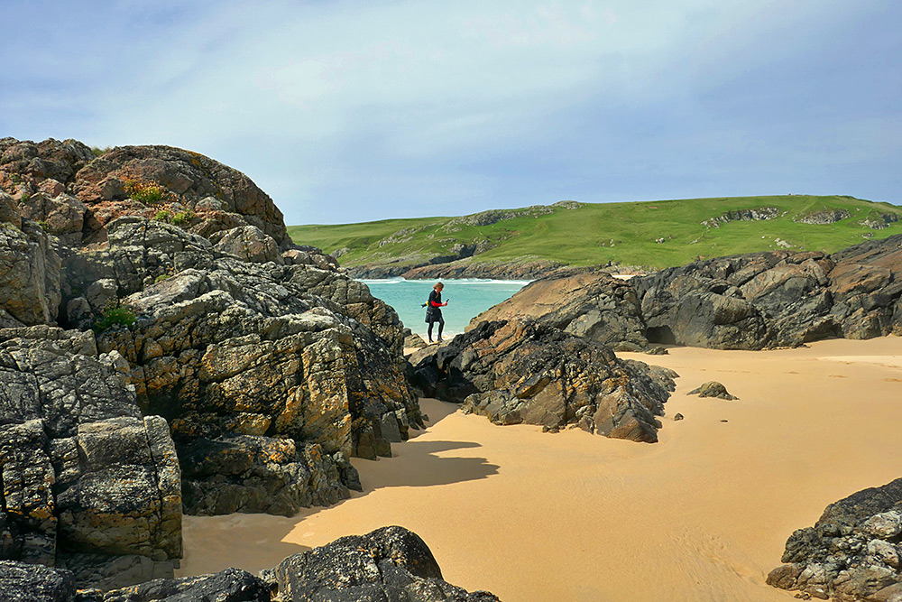 Picture of a person filming a video between large rocks on a sandy beach