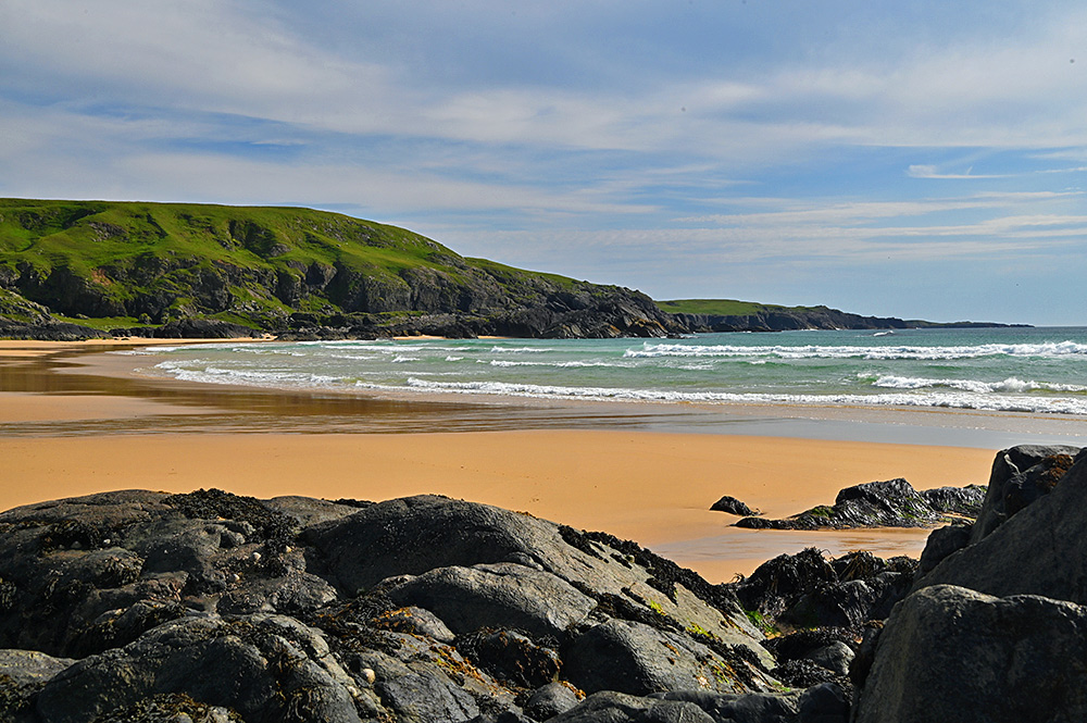 Picture of a bay with a sandy beach and a rocky coastline stretching into the distance