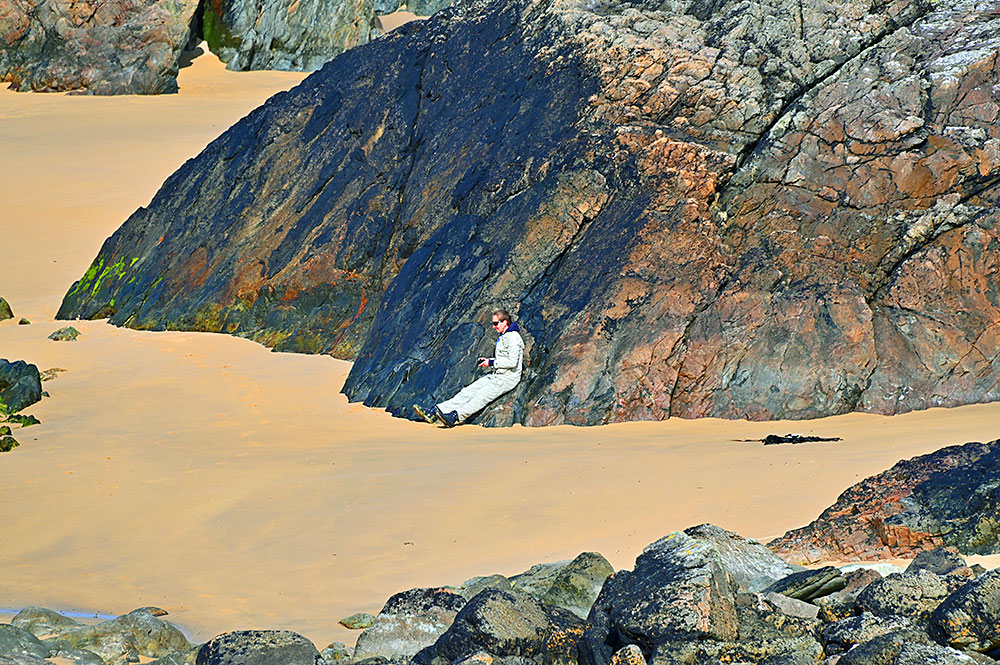 Picture of a woman sitting on the side of a large rock on a sandy beach