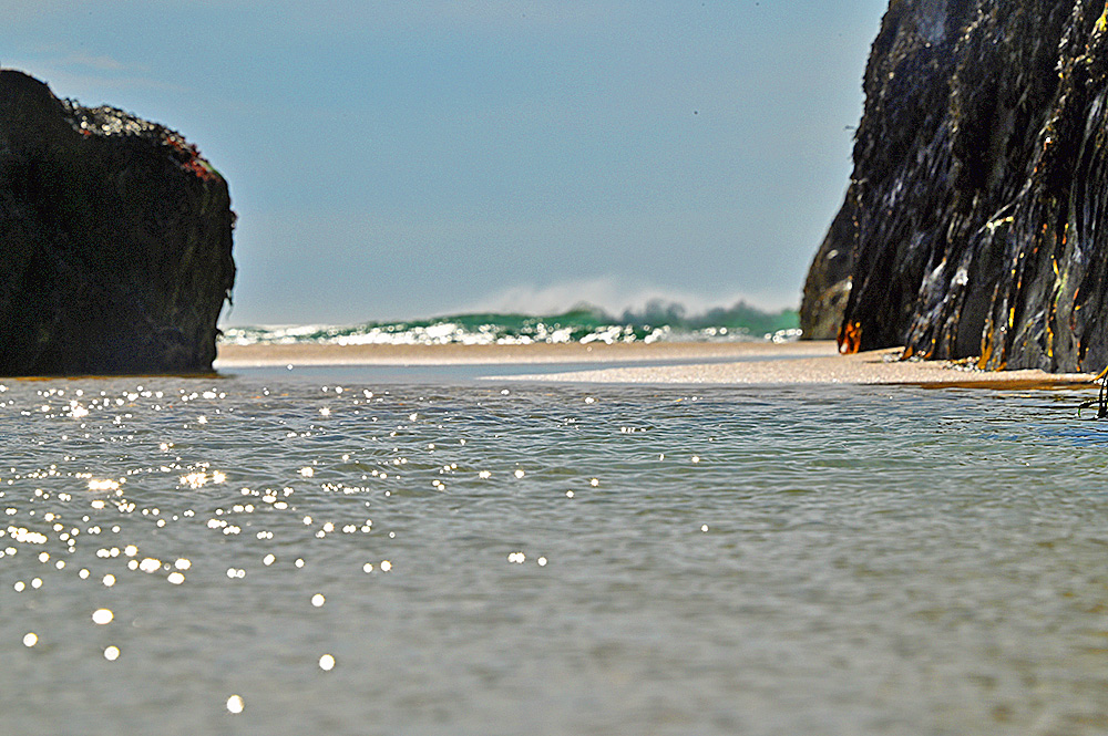 Picture of shallow water, some sand and a breaking wave flanked by dark rocks