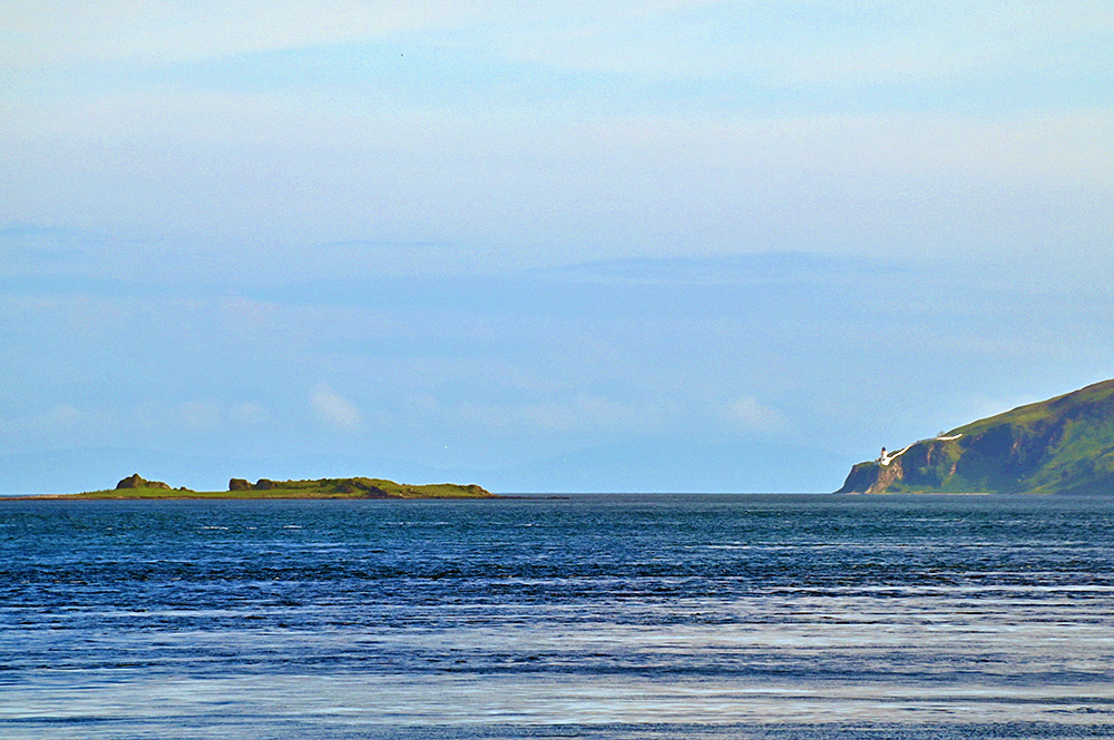 Picture of a small island and a lighthouse on a coastal cliff, seen down a sound between two islands