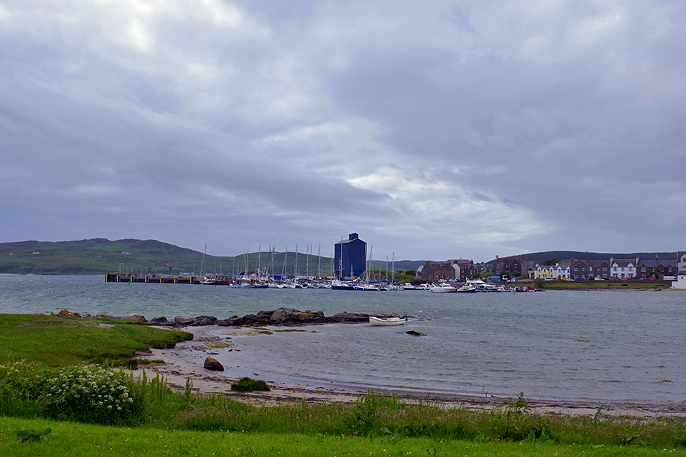 Picture of a view over a small sea loch in a coastal village, a pier with a grain silo and a marina on the other side