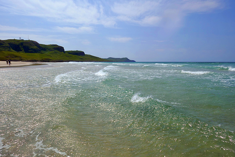 Picture of waves in a wide bay with a sandy beach, some walkers on the beach