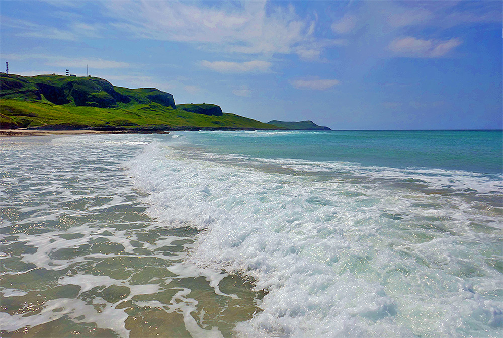 Picture of a wave in a bay breaking as it reaches a beach