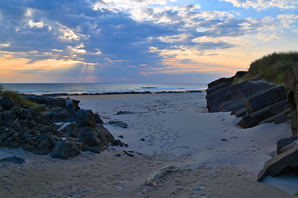 Picture of view over a sandy beach from between rocks and dunes on a summer evening with a dramatic sky
