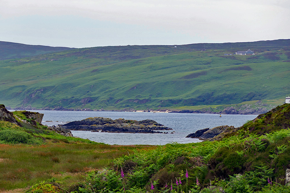 Picture of a distant small beach, seen across the water from a rugged coast