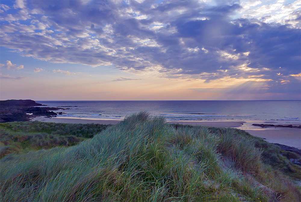 Picture of a view over a bay with a sandy beach from near the top of a dune