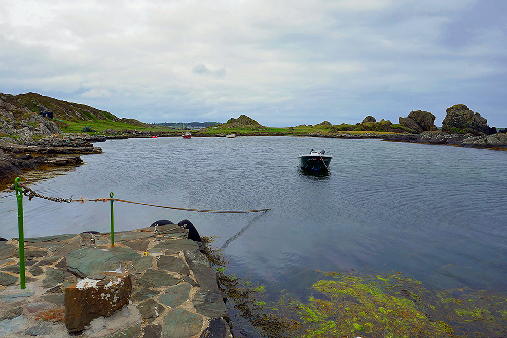 Picture of a natural harbour with some small boats, a coastal distillery in the distance