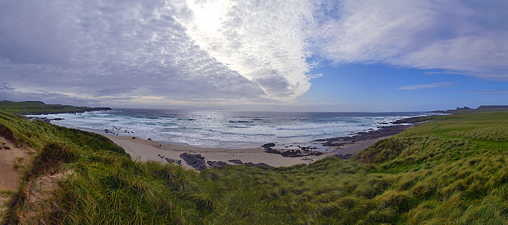 Panoramic picture of a view over a bay with a sandy beach, a weather front moving in from the left