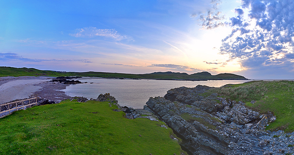 Panoramic picture of a small bay with a beach as well as some steep cliffs on a summer evening with sunset approaching