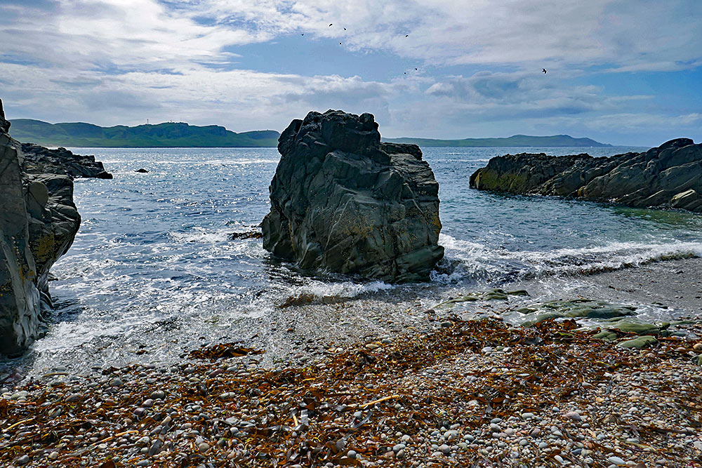 Picture of a big lump of rock in the centre of a small inlet with a stony beach
