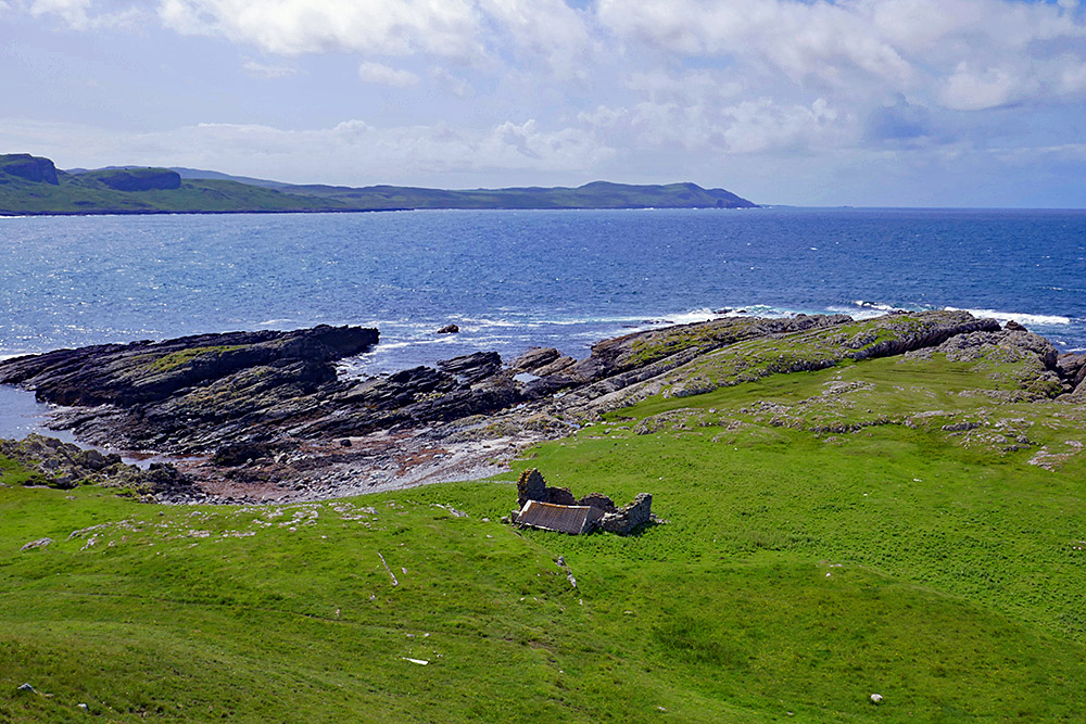 Picture of a small ruin with the roof blown off above a rocky shore next to a wide bay