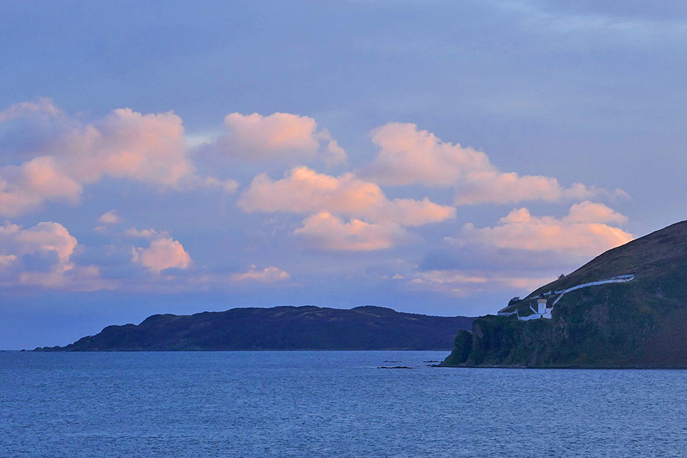 Picture of some colourful sunset clouds over a rugged coastal landscape with a white lighthouse