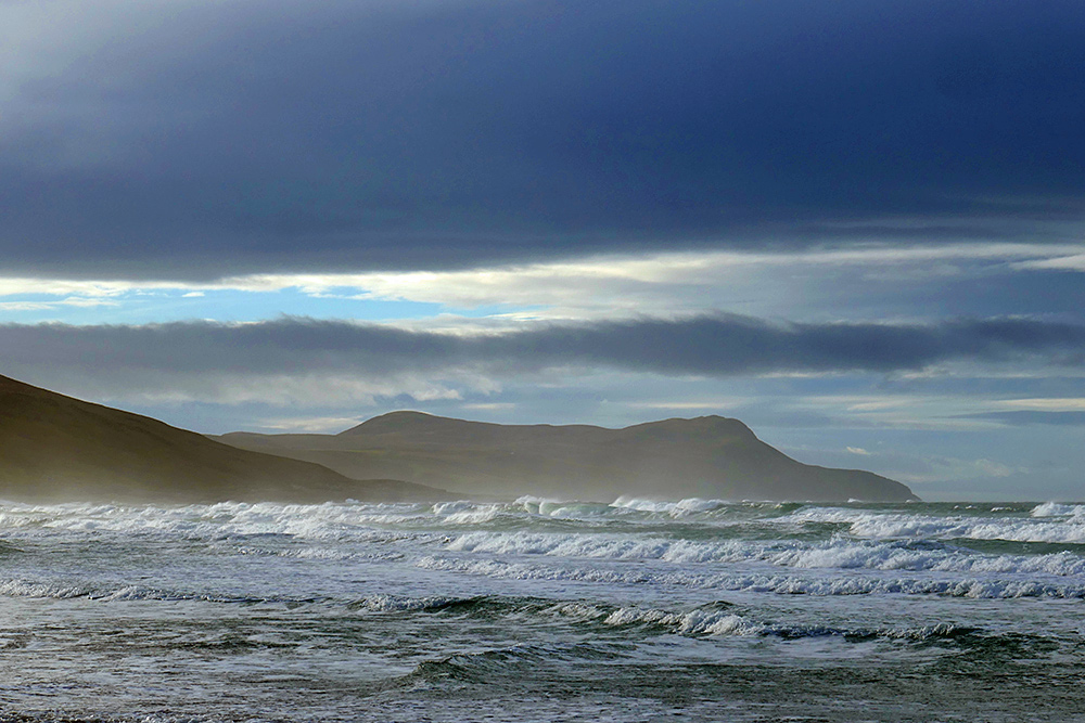 Picture of a bay with breaking waves, some dramatic dark clouds overhead