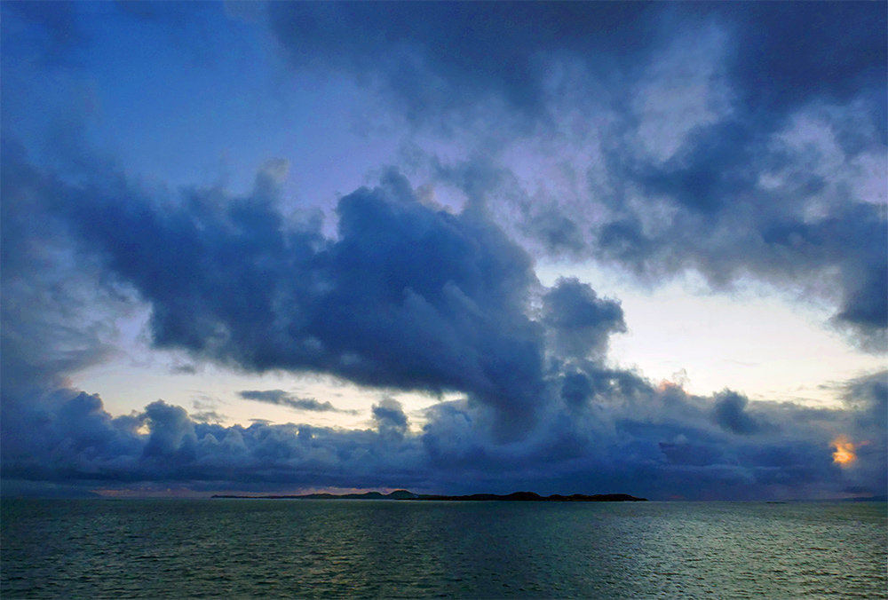 Picture of some dramatic clouds over an island, seen across the water from a ferry