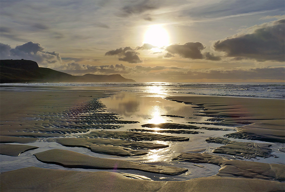 Picture of a hazy low sun over a bay with a golden sandy beach