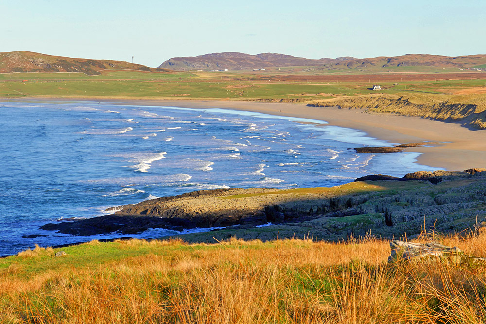 Picture of a wide sandy beach in a west coast bay, seen from a hillside above it