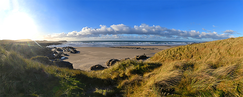Panoramic picture of a wide bay with a sandy beach and rocky outcrops seen from the dunes above the beach
