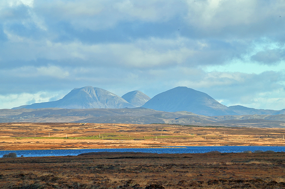 Picture of three rounded mountains seen across a rugged landscape with a freshwater loch