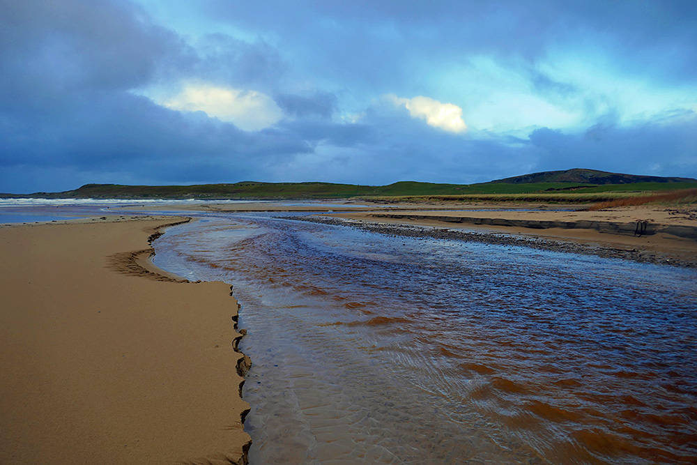 Picture of two burns (streams) flowing across a beach, joining before flowing into the sea