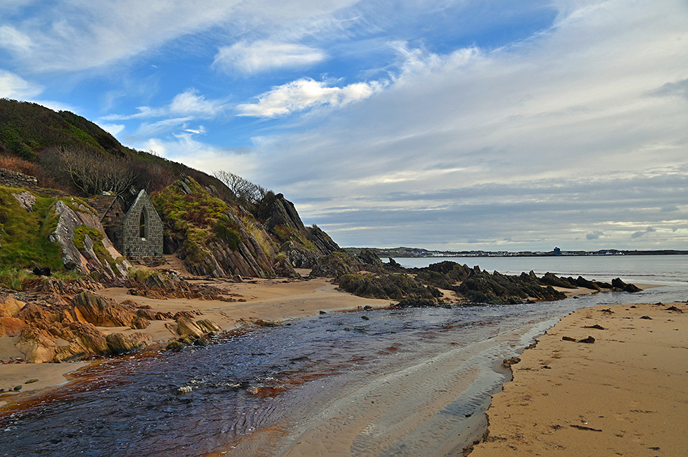 Picture of a stream running over a beach with the ruins of an old bathing hut behind