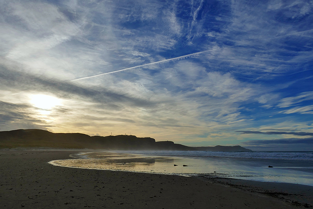 Picture of a dramatic cloudy and colourful sky over a sandy beach in a wide bay