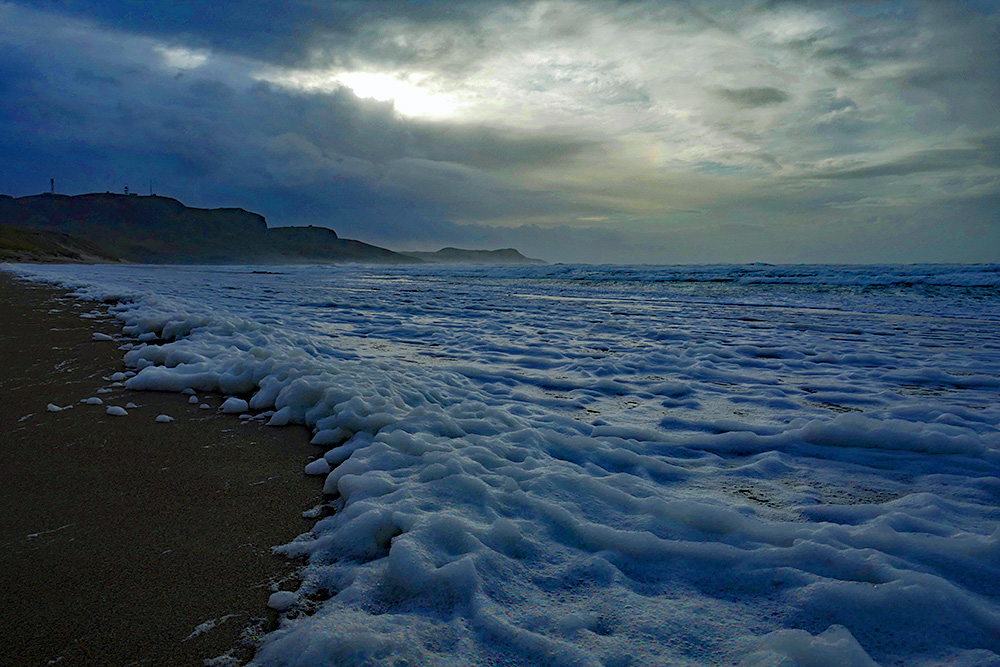 Picture of sea foam on a sandy beach on a stormy dark November afternoon with dramatic clouds overhead