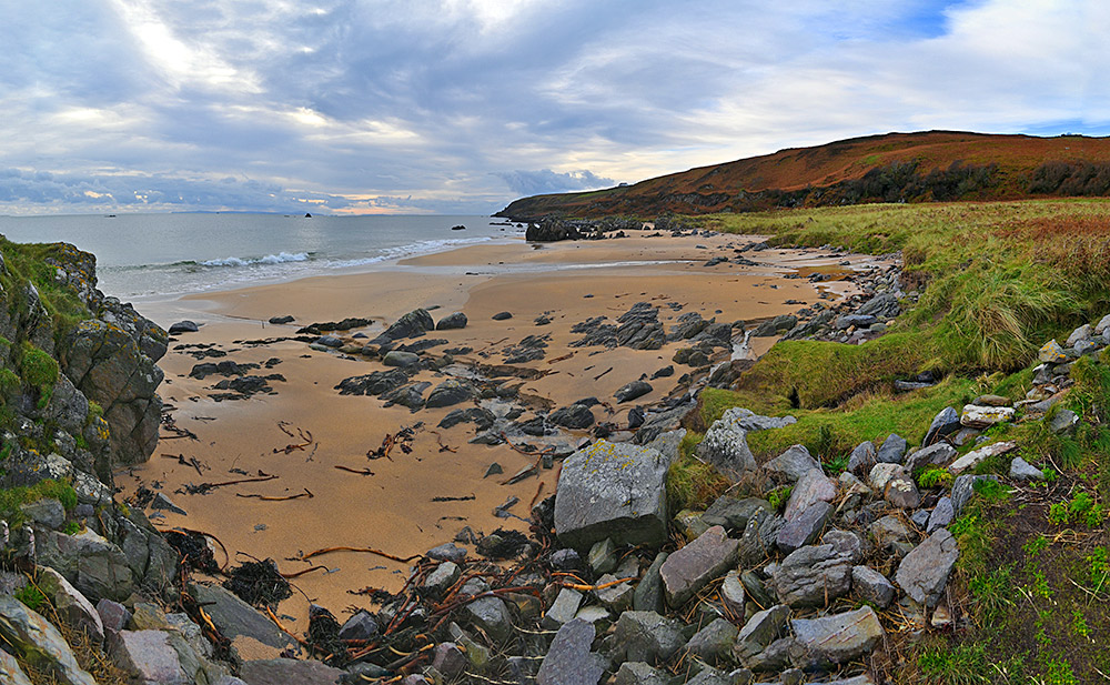 Panoramic picture of a sandy beach with some rocks strewn around, also some rocky outcrops