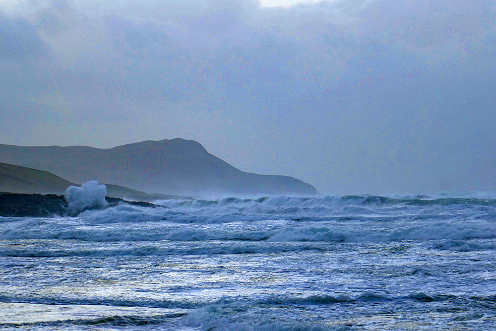 Picture of big storm waves rolling into a bay with cliffs and a beach