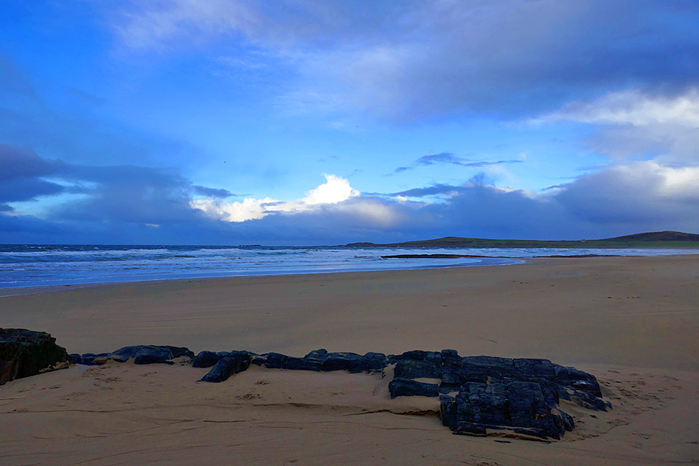 Picture of clouds breaking up over a bay with a sandy beach