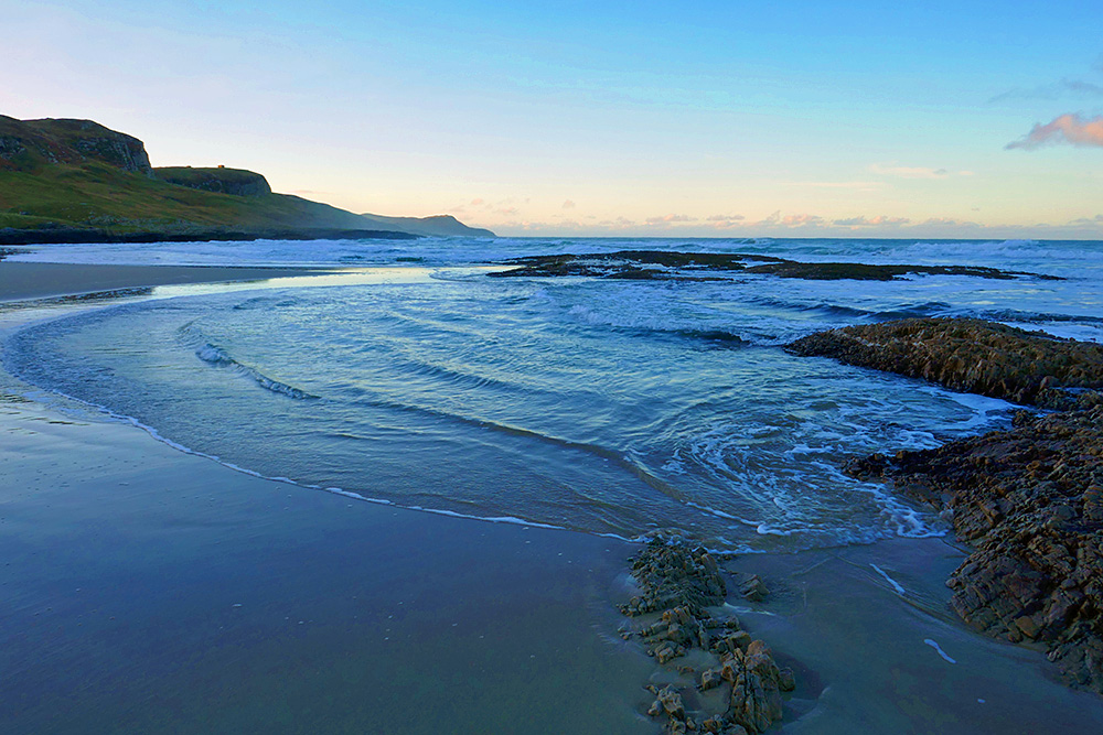 Picture of an incoming tide flowing through a rocky outcrop on a sandy beach
