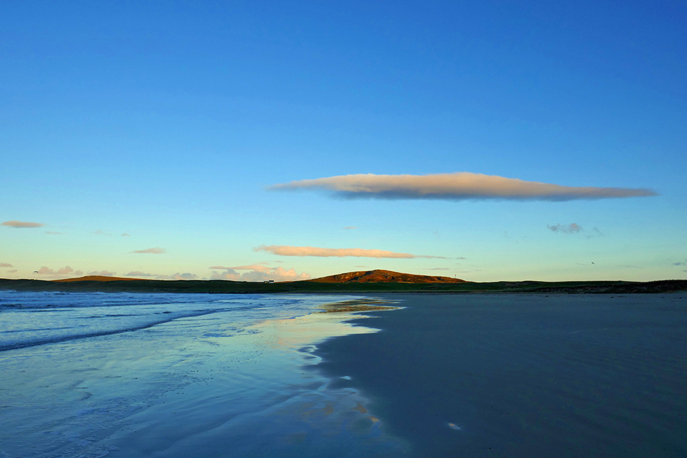 Picture of a view up a beach with a small hill in the mild morning sun at the end