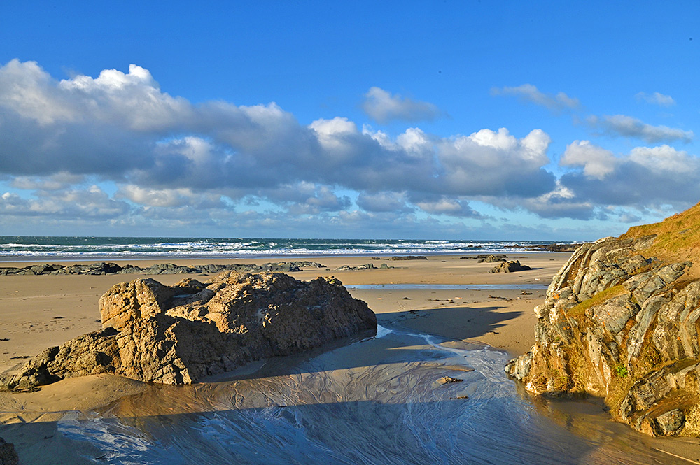 Picture of a view over a sandy beach with various rocky outcrops, waves rolling into the bay under a band of clouds moving in