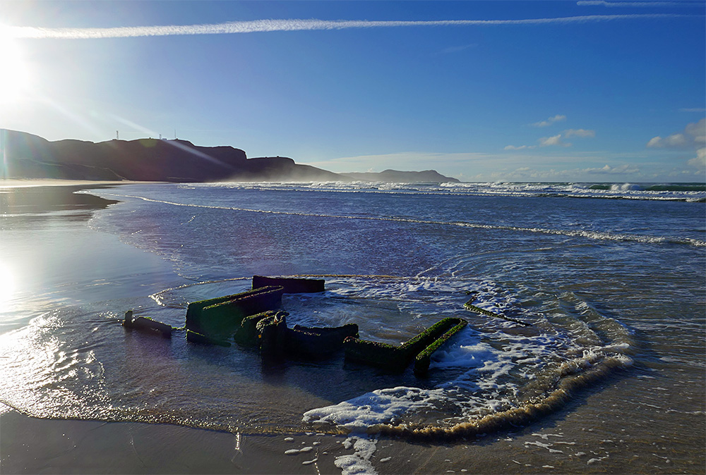 Picture of the remains of a wreck on a beach with waves from the incoming tide swirling around it