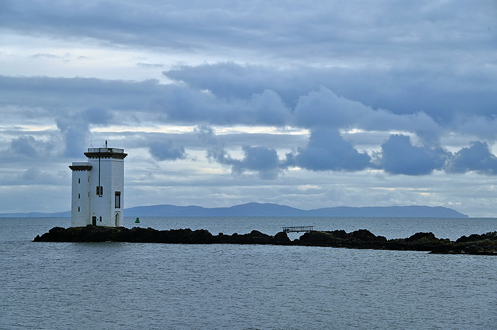 Picture of a square lighthouse on a rocky outcrop, a peninsula visible in the background