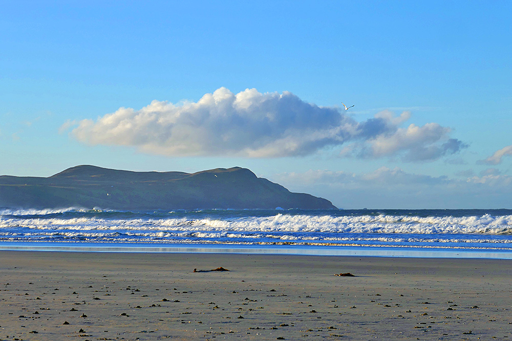Picture of a large cloud low over some coastal hills seen from a sandy beach